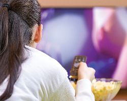 View of a woman holding a remote facing a large TV screen and a bowl of popcorn