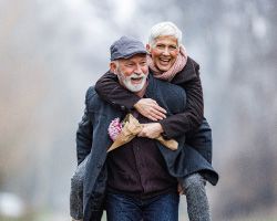  Two warmly-dressed seniors laugh outdoors.