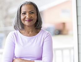 A woman smiling from her front porch.