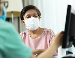 A patient and a provider wearing face masks look at a computer screen together.