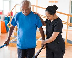 A physical therapist helps an older man with a walking exercise.