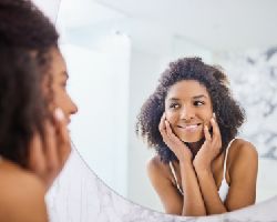 A woman looks in the mirror while touching her face.