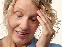 : A woman with her eyes closed and her hand pressed against the side of her head.
