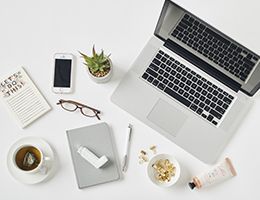 A laptop, cellphone, cup of tea, notebook and inhaler.