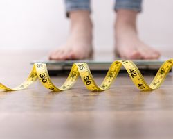 The feet of a woman standing on a scale with a tape measure in front of the scale.