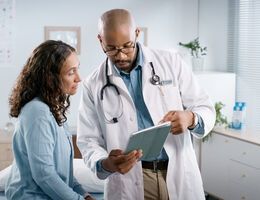 A woman and her doctor look at a tablet.