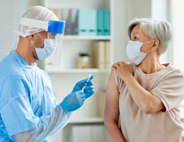 A healthcare worker prepares to give an older woman a shot.