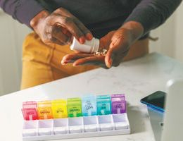 Hands shake pills from a bottle to place in a weekly organizer.