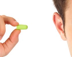 A hand holds a foam earplug near a man's ear.