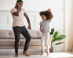 A father and young daughter dancing in the living room.