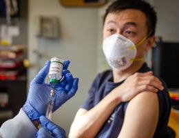 A man in a face mask rolls up his sleeve for a vaccine.