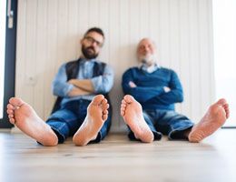 A father and adult son sit with the bottoms of their bare feet facing the camera