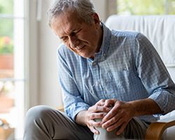 An older man grimaces as he holds his knee.