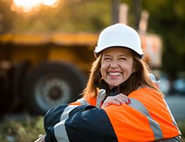 A smiling woman in a hard hat and orange jacket.