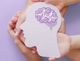 Hands hold a cut-out of a head with an EEG line over a stylized brain.
