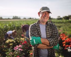 Man crossing his arms, smiling and standing in front of flower beds.