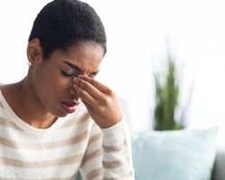 A photo of a woman grimacing and putting a hand to her face.