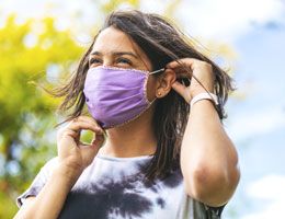 A woman puts on a cloth face mask.