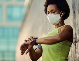 A masked woman wearing a tank top looks at her watch.