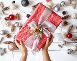 Hands display a wrapped gift in front of an array of Christmas decorations.