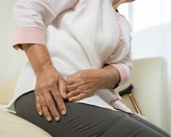 A seated person with their hands on their hip as if in pain.