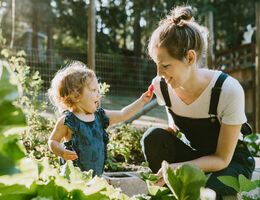 A woman and a toddler kneel in a garden.