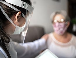 A healthcare worker in a mask and face shield touches the shoulder of a masked patient.