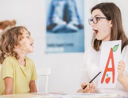 A teacher displays a card with the letter A on it to a laughing child.
