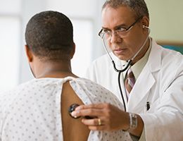 A doctor is using a stethoscope to listen to a man's lungs.