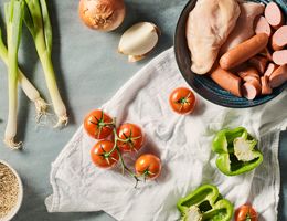 Sausage and chicken in a bowl, surrounded by an onion, tomato, and bell pepper.