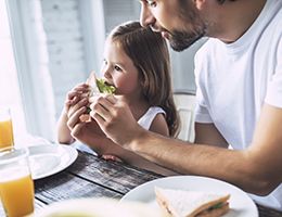 A father helps a child eat sandwich with lettuce.