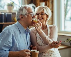 Older woman feeding avocado toast to spouse.