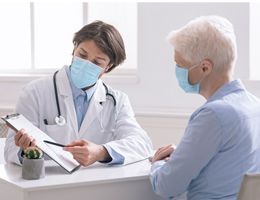 A masked healthcare worker and patient look at a clipboard together.