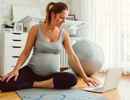 A pregnant woman sits on the floor and looks at a laptop.