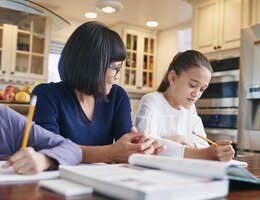 Kids doing homework at a table while a parent watches