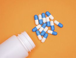 Open pill bottle with blue and white capsule pills spilling out.