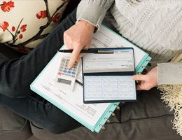 A view of someone's lap from above with a checkbook, calculator and notebook.