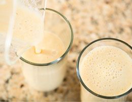 Mango shake being poured from a pitcher into two tall glasses.