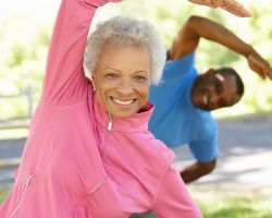 A smiling woman stretches her arm overhead. Behind her, a man does the same.