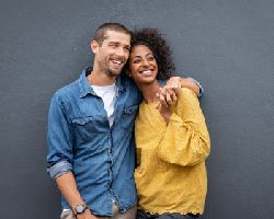 A smiling couple leans against a wall.