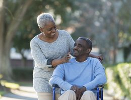 A woman smiles as she pushes a smiling man's wheelchair