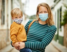A woman and a toddler wearing masks outside.