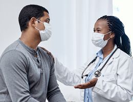 A masked doctor talks to her masked patient.