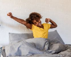 A teenaged girl stretches and smiles in bed