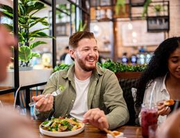 A smiling man eats a salad in a restaurant.