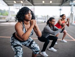 A row of people do squats on an outdoor basketball court.
