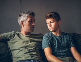 A father and son sitting looking somber.