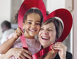 A woman and child smile through a red heart-shaped cutout.