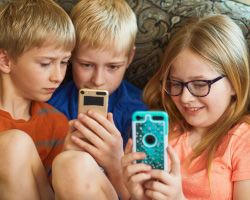 Three kids gather around their smartphones.