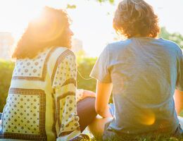 Two people sit outside in the sun, talking.